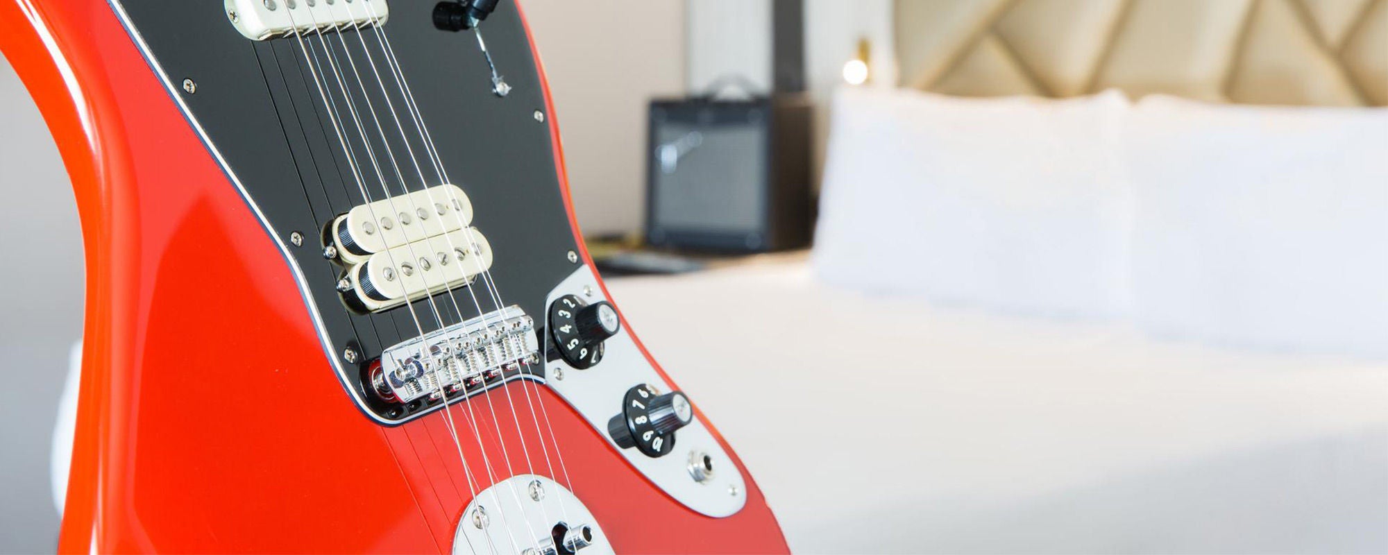 red guitar leaning on bed
