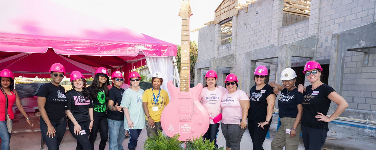 group of people wearing pink construction hats with a giant guitar